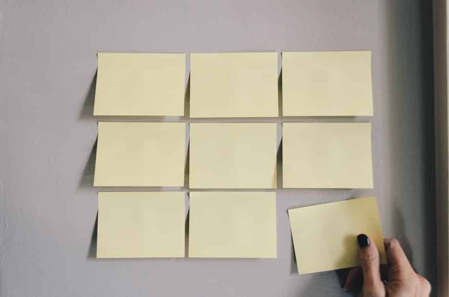 Fotografia de uma pessoa retirando uma folha de bloco de notas em branco de uma parede também composta por outras idênticas a mesma.