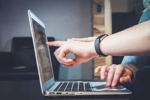 Fotografia de duas pessoas mexendo em um notebook. Enquanto uma mão aperta o touchpad, a outra indica algo na tela.