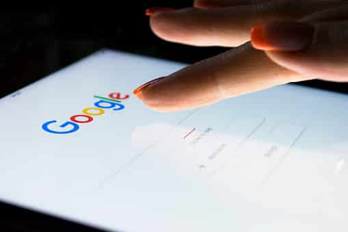 Imagem de uma mão posicionada próxima à palavra Google, na tela de um smartphone.