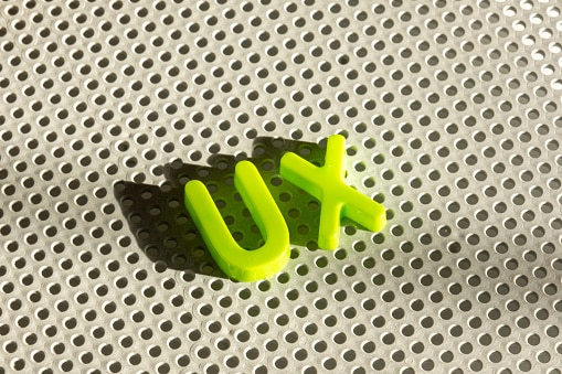 Fotografia das letras que formam a palavra UX em um fundo branco com várias perfurações.